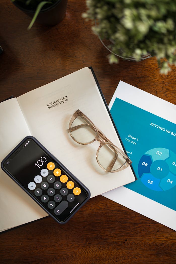 Top view of business planning essentials on a desk with smartphone calculator and eyeglasses.